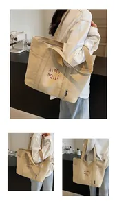 Dettaglio della borsa tote in tela beige con ricamo rosso e lunghi manici a spalla