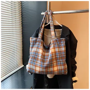 Detail of blue and orange plaid tote bag with heart button on a clothing rack