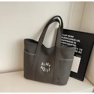 Dettaglio della borsa tote in tela grigia con tasche laterali e stampa del logo minimal
