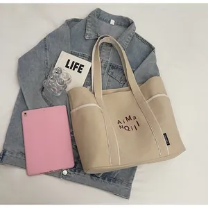 Dettaglio della borsa tote in tela beige con ricamo rosso ed etichetta su sfondo denim