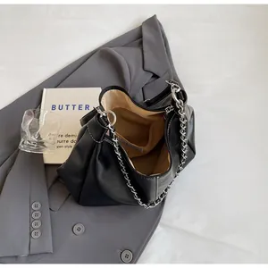 Details einer schwarzen Plissee-Schultertasche mit silberner Kette auf grauem Blazer