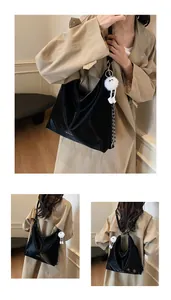 Détail d'un grand sac noir avec breloque monstre en peluche blanche et chaîne argentée