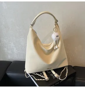 Détail du sac seau blanc crème avec chaîne, logo métallique et breloque en peluche