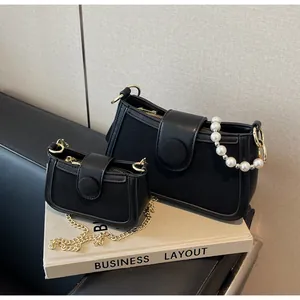 Détail de sacs bandoulière noirs avec chaîne en perles blanches et bandoulière dorée