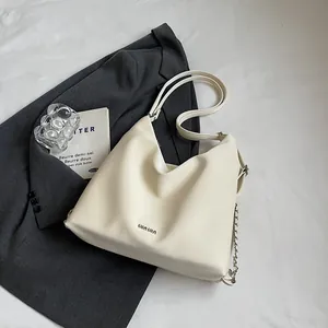 Sac seau blanc crème avec chaîne et logo WAWA en métal sur fond de blazer gris foncé chic