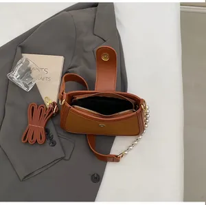Vue détaillée du sac sous le bras en cuir marron avec chaîne en perles sur veste