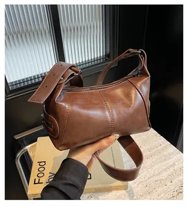 Detail view of deep brown faux leather shoulder bag with decorative eyelet strap and zippers
