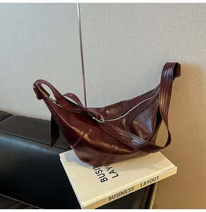 Nahaufnahme einer weinroten sichelförmigen Ledertasche mit Falten auf einem Buch