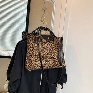 Modische Leoparden-Einkaufstasche mit schwarzen Griffen und Anhängern vor weißer Wand