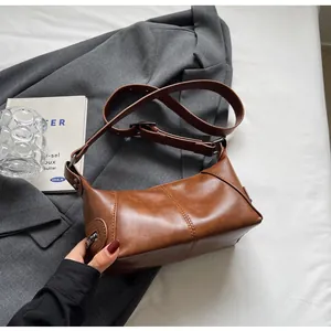 Detail of vintage brown leather underarm bag featuring vertical stitching and adjustable strap