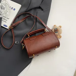 Retro braune Zylindertasche mit Plüsch-Anhänger auf stilvollem grauem Anzug-Hintergrund