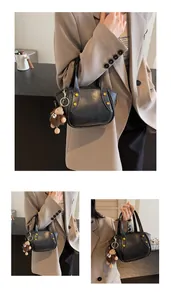 Detail der schwarzen Leder-Eimertasche mit dekorativen Punkten und Plüschbär-Anhänger