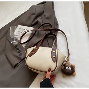 Detail der weichen cremefarbenen Beuteltasche mit braunen Griffen und Monster-Anhänger