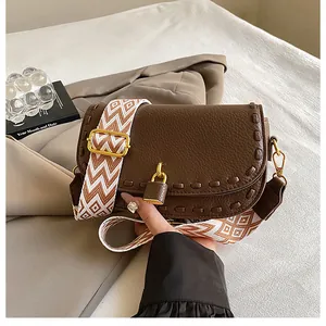 Détail du sac en cuir marron foncé avec bandoulière tissée large et fermoir doré