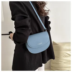 Gros plan d'un sac selle bleu clair porté par un mannequin en blazer noir chic