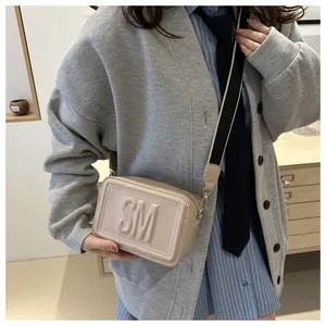 Detail der beige quadratische Umhängetasche mit SM-Relieflogo und breitem Gurt