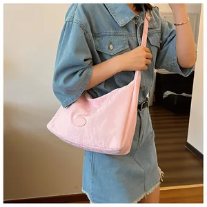Pale pink crescent bag with crinkle texture worn cross-body over a blue denim dress