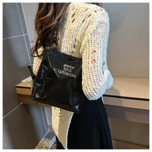 Detail of glossy black pleated tote bag with white embroidery on polished faux leather