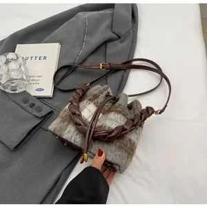 Détail du sac seau en laine à carreaux avec poignée tressée sur un blazer gris chic