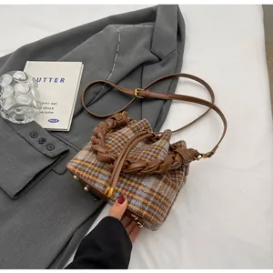 Détail du sac seau à carreaux rétro avec anse tressée et rivets dorés sur veste grise