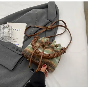 Détail du sac seau en laine à carreaux avec poignée tressée et pieds en métal