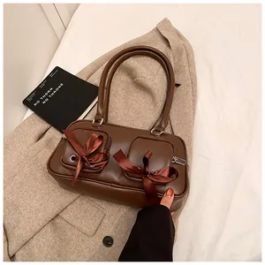 Detail of a brown shoulder bag featuring ribbon bows and twin zipper pockets on PU leather