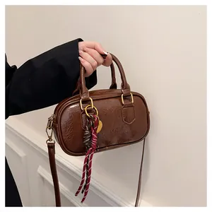 Détail d'un sac à main marron foncé à texture plissée avec ferrures dorées et breloque tressée