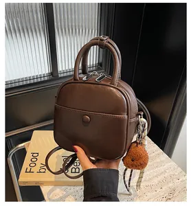 Détail d'un sac à bandoulière rétro marron foncé avec breloque ours et double fermeture éclair