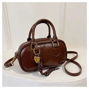 Détail d'un sac à main marron foncé brillant avec cadenas coeur doré et foulard en soie