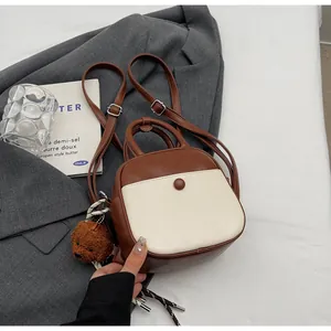 Détail d'un sac à dos rétro bicolore marron et crème avec un pendentif ours en peluche