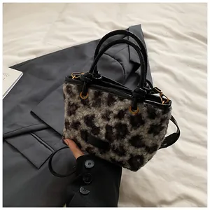 Detailed close-up of a leopard print plush handbag with black faux leather handles and gold metal hardware