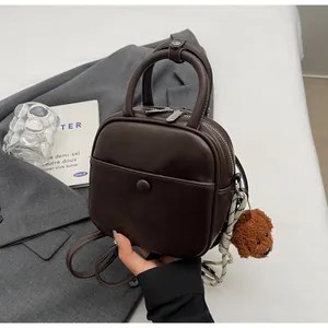 Détail d'un mini sac à dos en cuir marron avec breloque ours sur un blazer gris