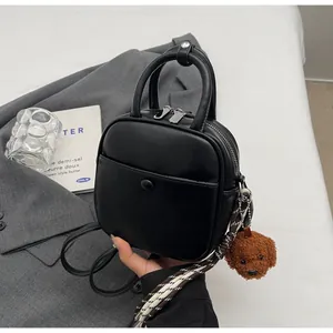 Détail du sac bandoulière en cuir noir avec breloque ours et lanière rayée stylée