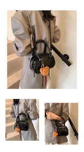 Detail of a black patent leather handbag with a plush bear charm and adjustable shoulder strap