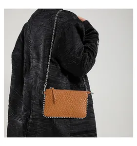 Detail of a brown woven crossbody bag with silver rivets and metal chain strap