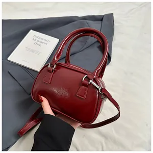 Detail of burgundy patent leather Boston bag held by hand against a grey blazer backdrop