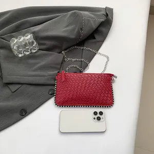 Red embossed crossbody bag with silver beaded trim and chain strap on desk