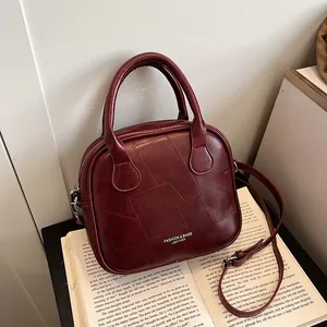 Vintage dunkelrote Lederhandtasche mit Patchwork-Design auf einem Buch liegend