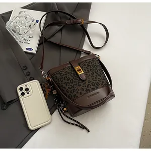 Sac seau léopard avec fermoir doré posé sur un blazer gris et des livres vintage