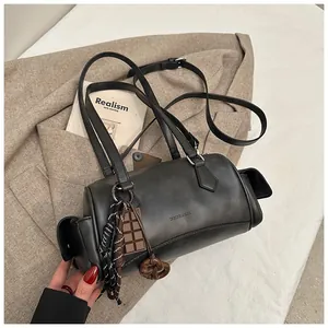 Détail d'un sac Boston cylindrique noir avec poches latérales et breloque chocolat
