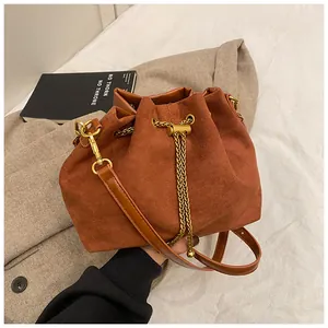Detail of tan suede bucket bag with gold chain and drawstring on a warm wool coat