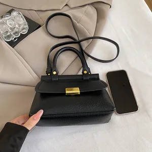 Mini sac carré noir en cuir grainé avec fermoir doré sur un trench-coat beige
