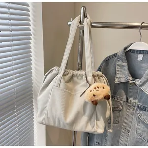 Detail of cream corduroy tote bag showing ribbed texture, drawstring and plush charm