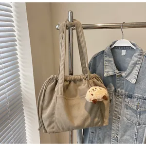 Detail of khaki corduroy tote bag featuring drawstring closure and fuzzy charm pendant
