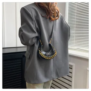 Detail einer schwarzen Halbmond-Tasche aus Leder mit goldener Kette an einem Modell