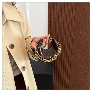 Detail einer dunkelbraunen Mini-Tasche aus glänzendem Lackleder mit goldener Gliederkette