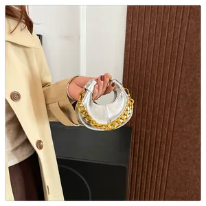 Detail der silbernen Halbmondtasche mit goldener Kette auf beigeem Mantel