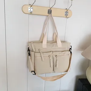 Cream colored multi-pocket nylon crossbody bag with adjustable strap and top handles
