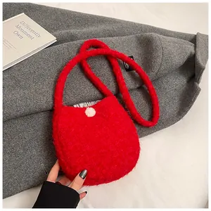 Gros plan d'un sac à bandoulière en peluche rouge avec un pompon blanc sur laine grise