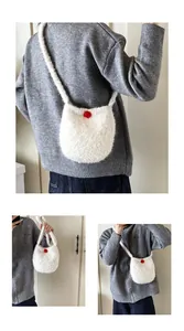 Détail d'un sac seau en peluche blanche avec un pompon décoratif rouge sur le devant